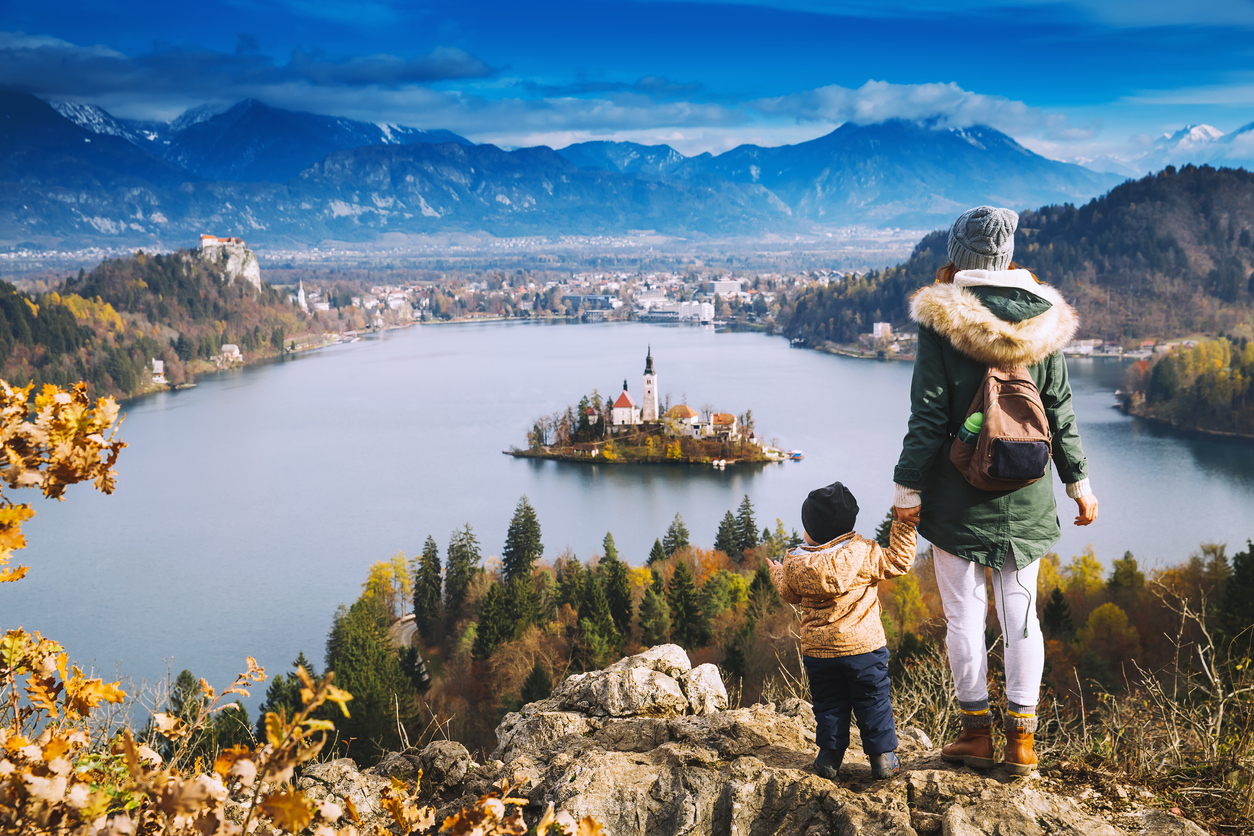 Family travel Europe. Mother with son looking on Bled Lake. Autumn or Winter in Slovenia, Europe. Top view on Island with Catholic Church in Bled Lake with Castle and Mountains in Background.